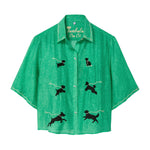 Green cropped cabana shirt with black dog silhouettes across the front, each attached to a white leash motif, with white piping along the collar and sleeves.