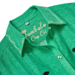 Close-up of a green cropped cabana shirt collar with white leash embroidery and “Tombolo Crop Cut” script stitched inside the neckline.