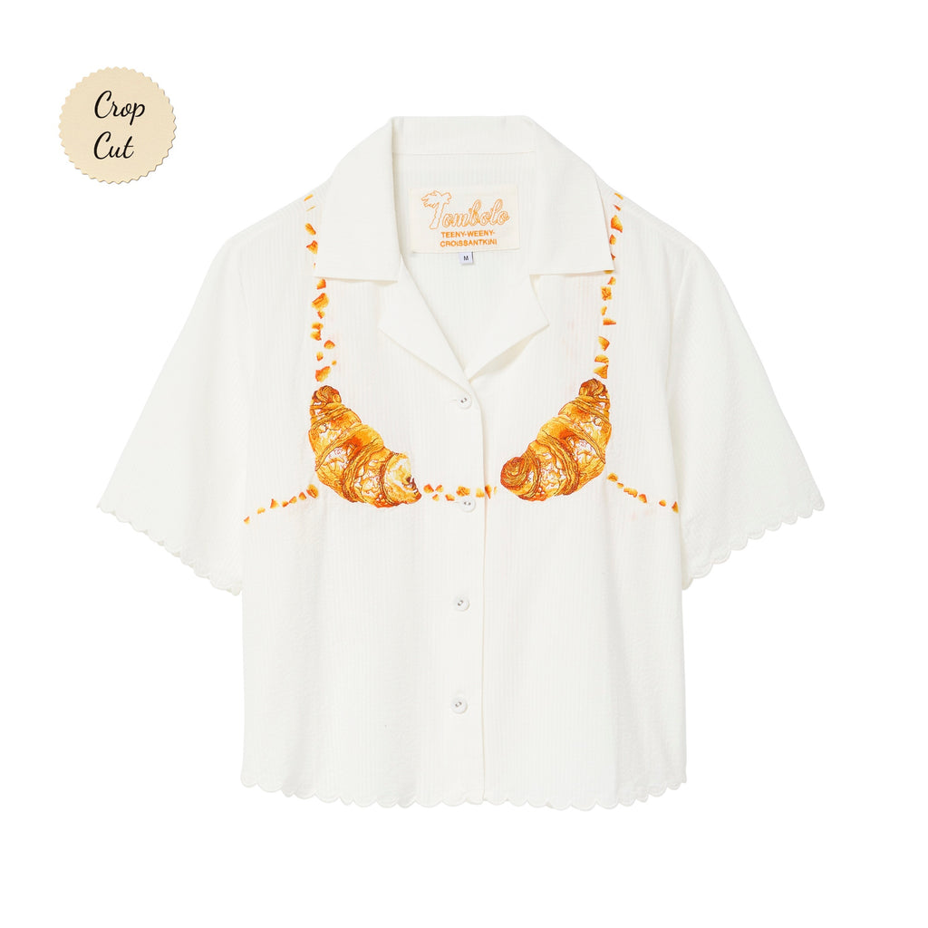 White cropped cabana shirt with printed golden croissants across the chest and scalloped edges.