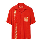 Red short-sleeve cabana shirt featuring an embroidered Negroni glass on the chest pocket and three twisted appliqué stripes running down one side. The shirt has matching red buttons and a chain-stitched “Tombolo” logo at the collar.

