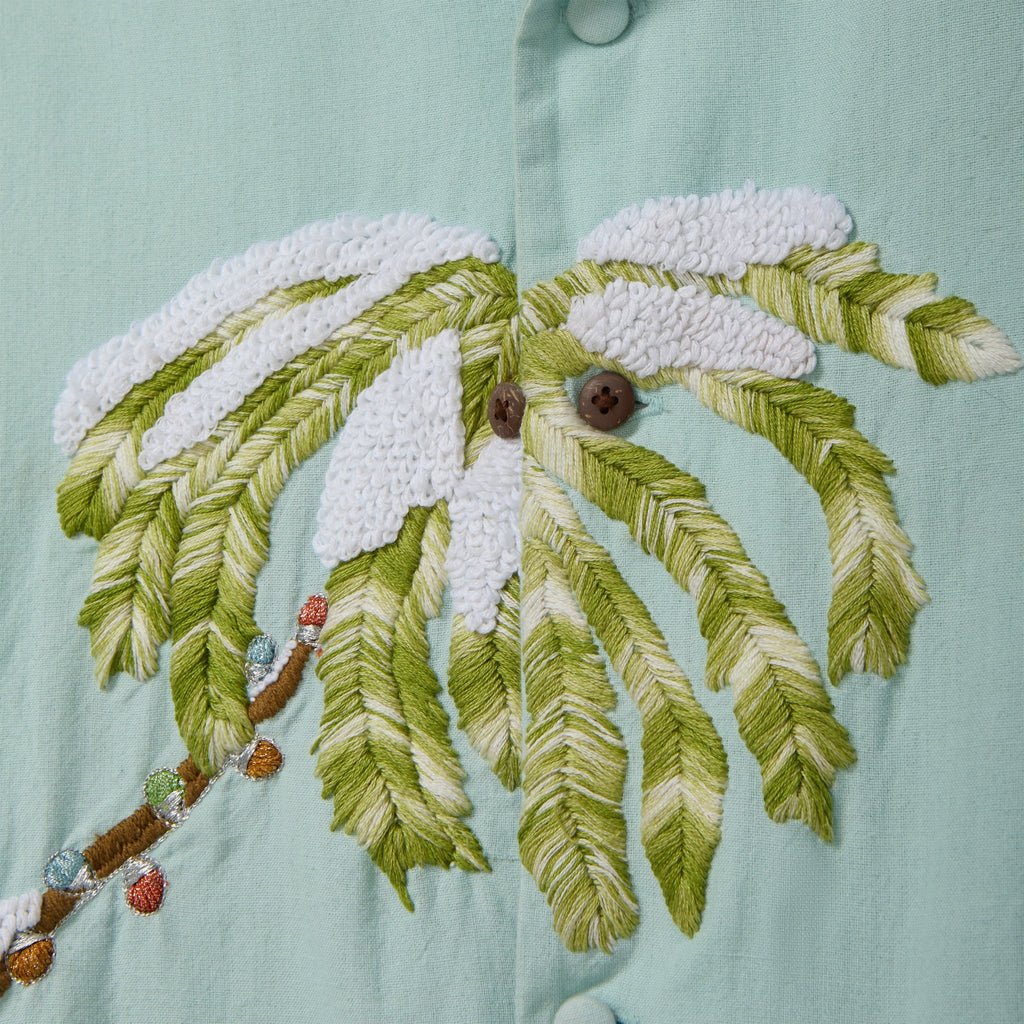 Close-up of a light blue cabana shirt showing embroidered palm tree fronds with white snowy accents and decorative multicolored lights along the trunk.