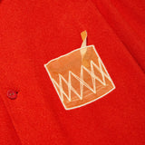 Close-up of a red cabana shirt showing an embroidered Negroni glass on the chest pocket, featuring a transparent mesh panel and a stitched orange garnish detail.