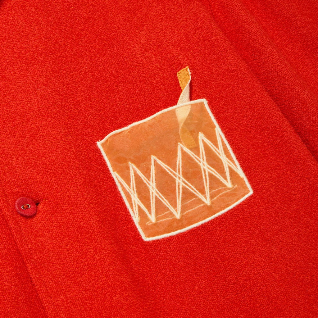 Close-up of a red cabana shirt showing an embroidered Negroni glass on the chest pocket, featuring a transparent mesh panel and a stitched orange garnish detail.