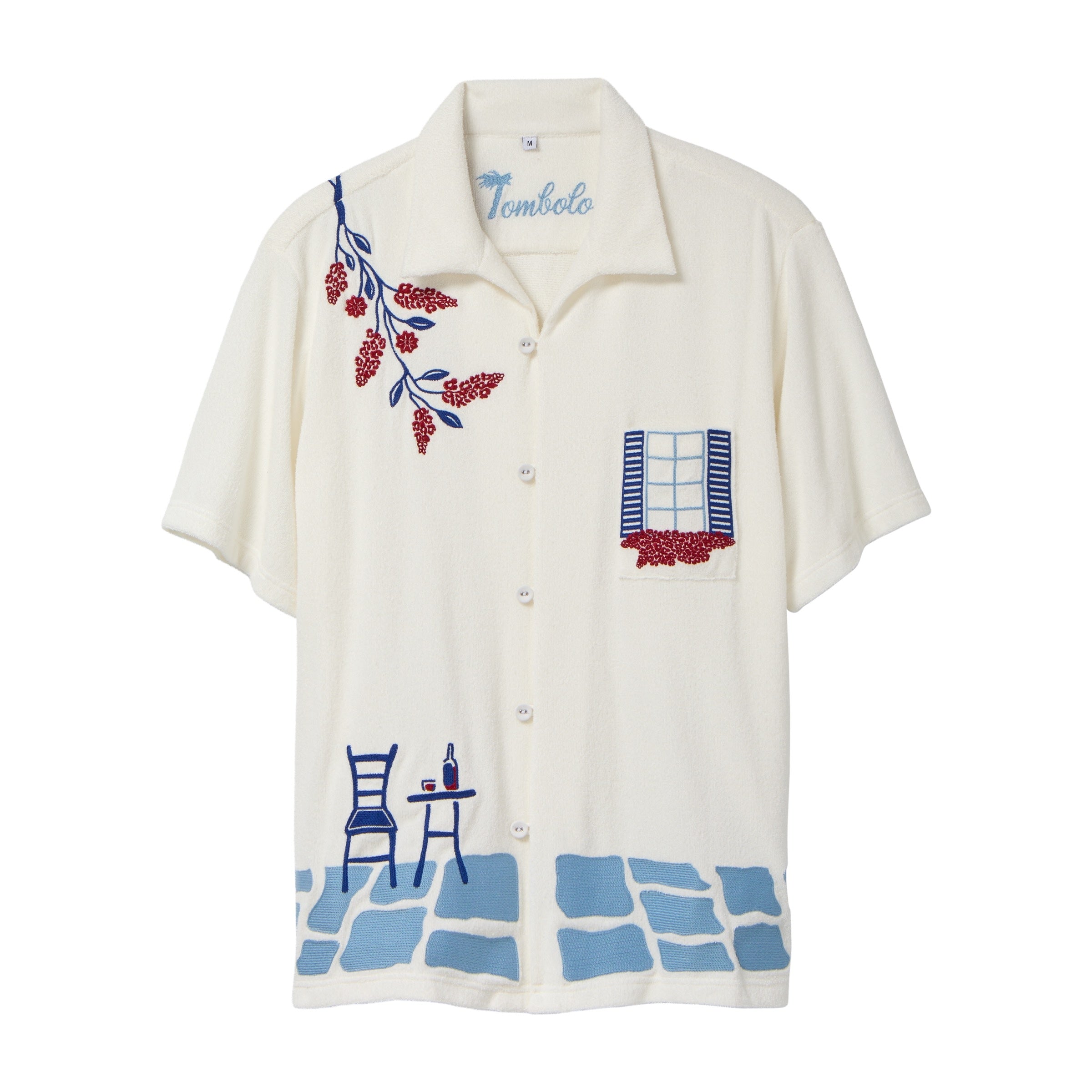 Cream terry cabana shirt with embroidered blue and red Mediterranean motifs, including flowers, a window, café table, chair, and cobblestone hem.
