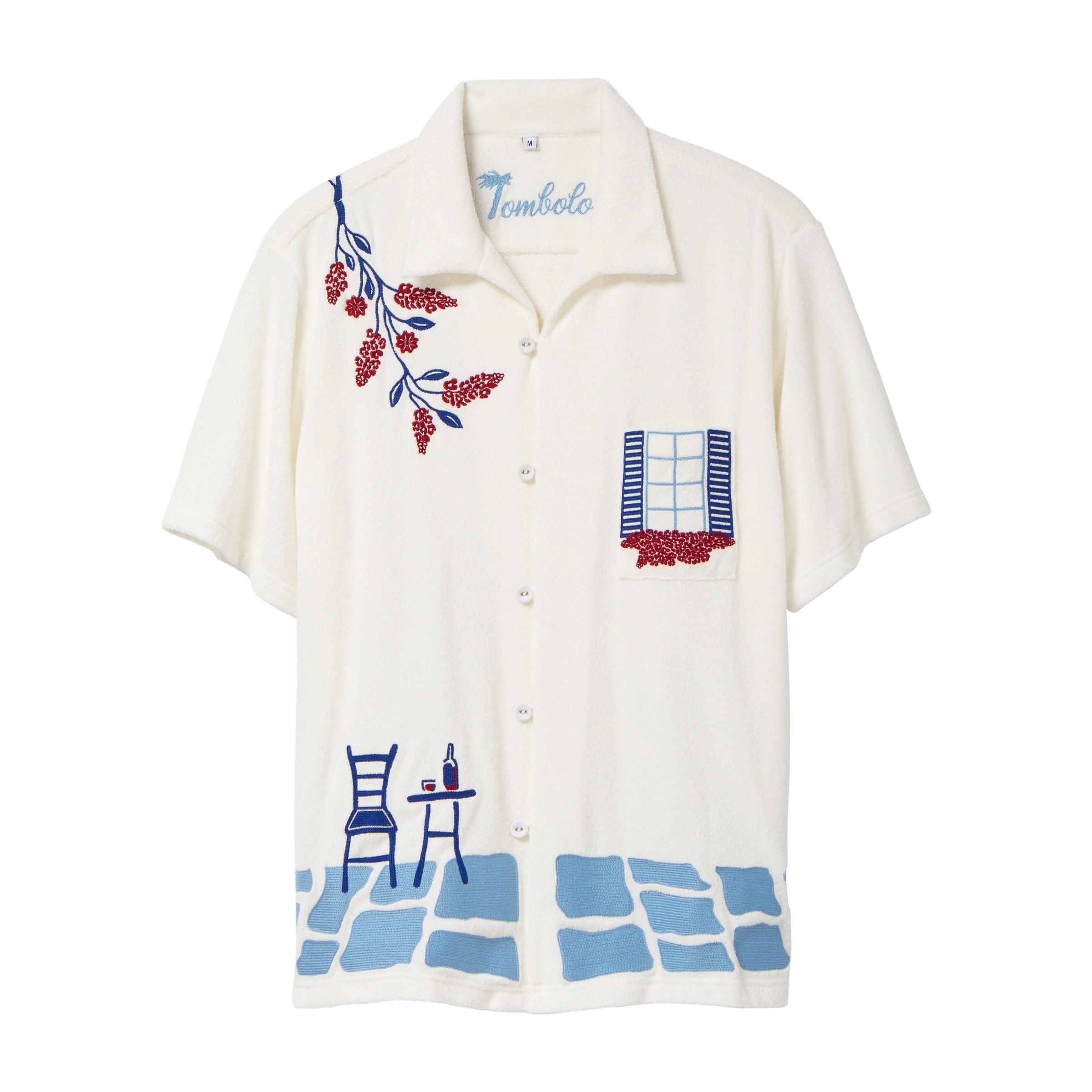 Cream terry cabana shirt with embroidered blue and red Mediterranean motifs, including flowers, a window, café table, chair, and cobblestone hem.
