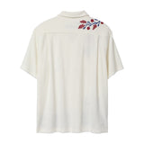 Back view of a cream terry cabana shirt with embroidered red floral vines and blue leaves on the shoulder.