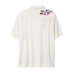 Back view of a cream terry cabana shirt with embroidered red floral vines and blue leaves on the shoulder.
