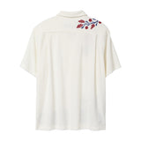 Back view of a cream terry cabana shirt with embroidered red floral vines and blue leaves on the shoulder.