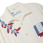 Close-up of a cream terry cabana shirt with embroidered floral vine and blue shuttered window pocket details.