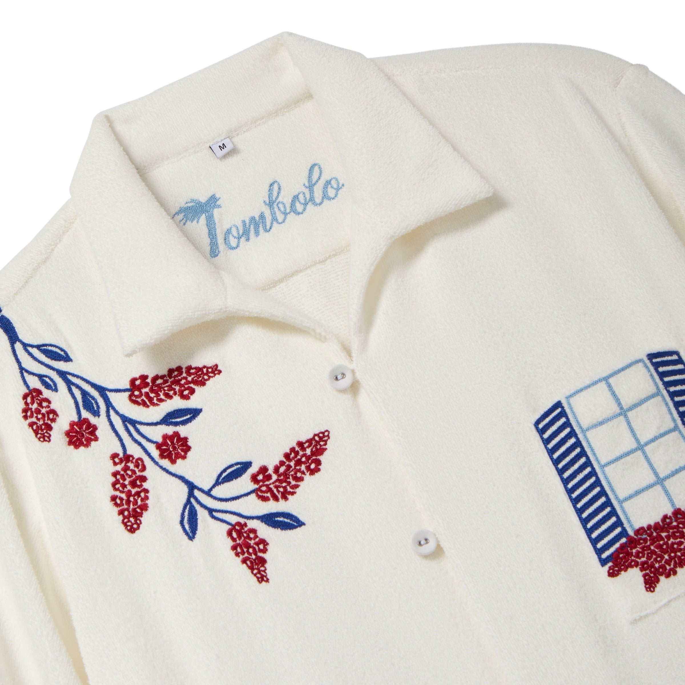 Close-up of a cream terry cabana shirt with embroidered floral vine and blue shuttered window pocket details.