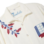 Close-up of a cream terry cabana shirt with embroidered floral vine and blue shuttered window pocket details.