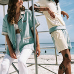 man and woman laughing and casualy leaning on lifeguard chair at the beach, wearing the terrycloth and line oyster shirts