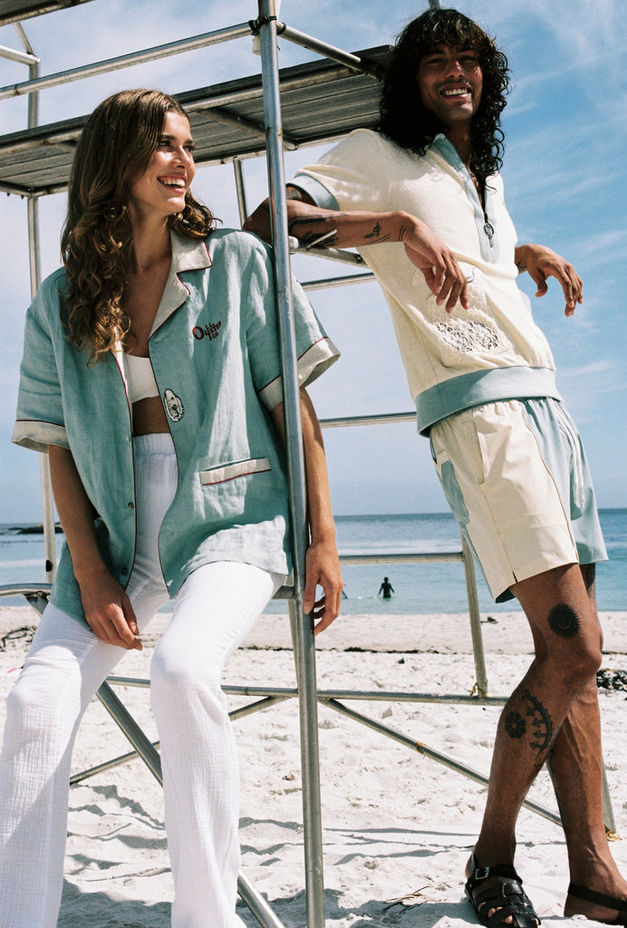 man and woman laughing and casualy leaning on lifeguard chair at the beach, wearing the terrycloth and line oyster shirts