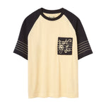 Short-sleeve raglan terry shirt with cream body, black sleeves, and SNL-embroidered chest pocket.