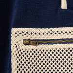Close-up of a navy blue fabric with a gold zipper and beige crochet border.