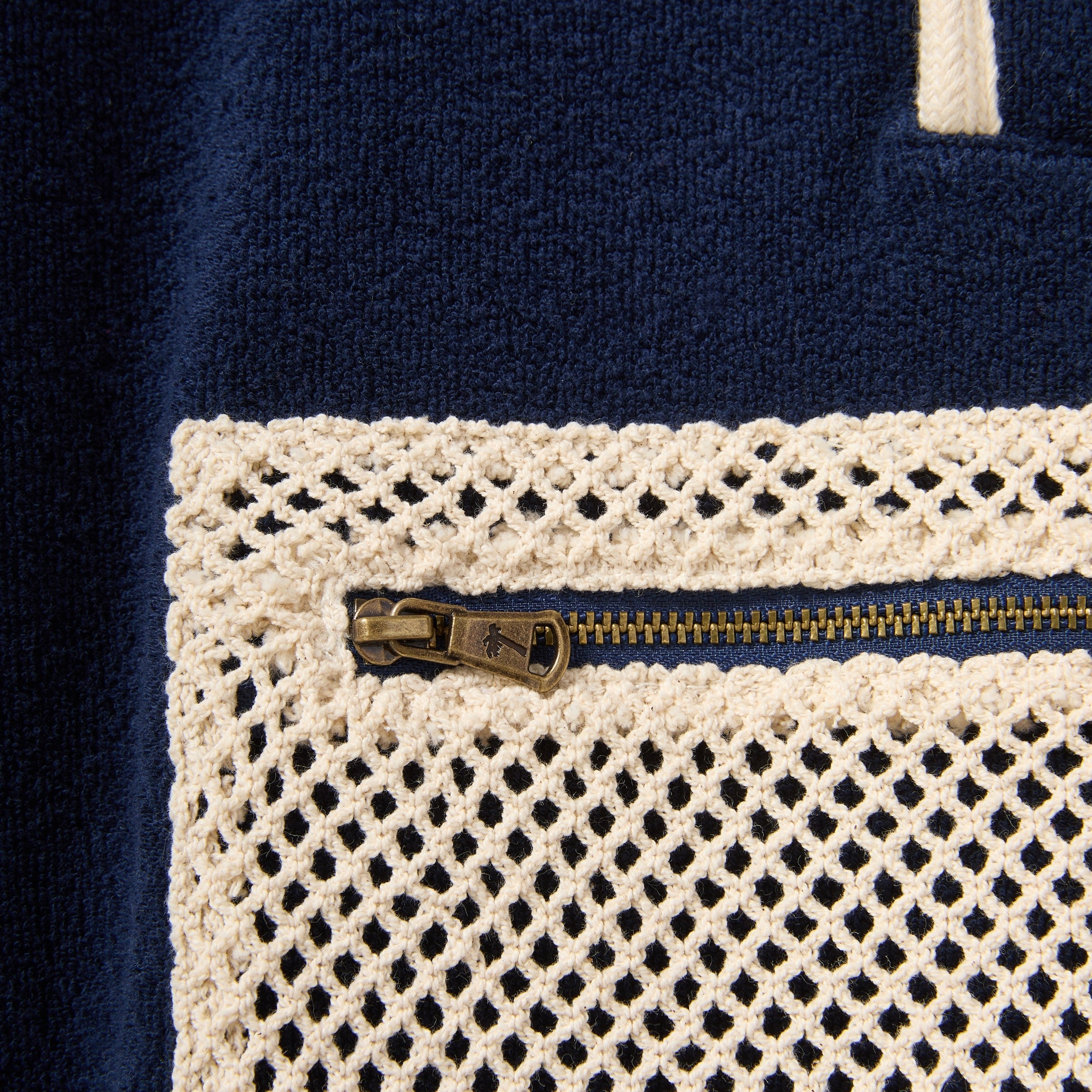 Close-up of a navy blue fabric with a gold zipper and beige crochet border.