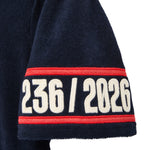 Close-up of navy blue terry shirt sleeve with red border and white text '236/2026'.