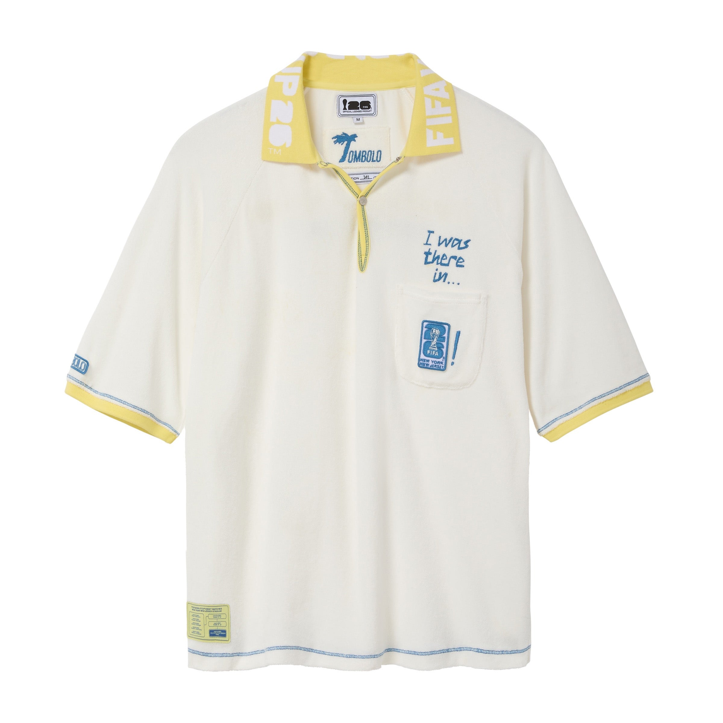 Cream terry cloth polo shirt with a yellow contrast collar, blue contrast stitching, embroidered “I was there in…” text, chest pocket with FIFA World Cup New York New Jersey patch, and FIFA World Cup sleeve patch.
