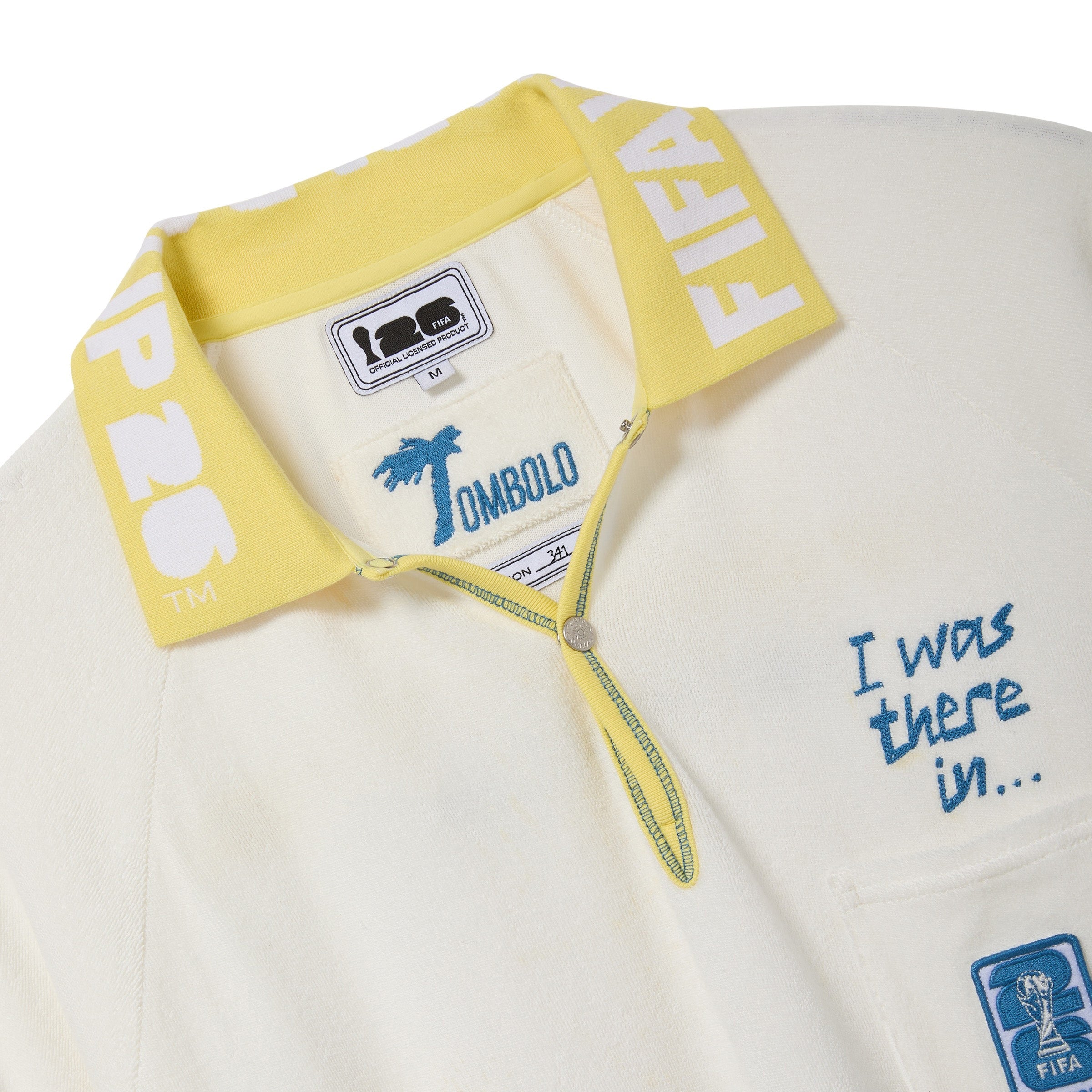 Close-up of a white polo shirt with yellow collar and text, featuring the FIFA 26 interior label.