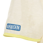 Close-up of a beige garment with a blue 'Tombolo' logo on a white background