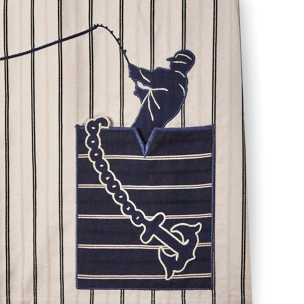 Close up of striped shirt with navy pocket Graphic of man fishing and anchor across the pocket