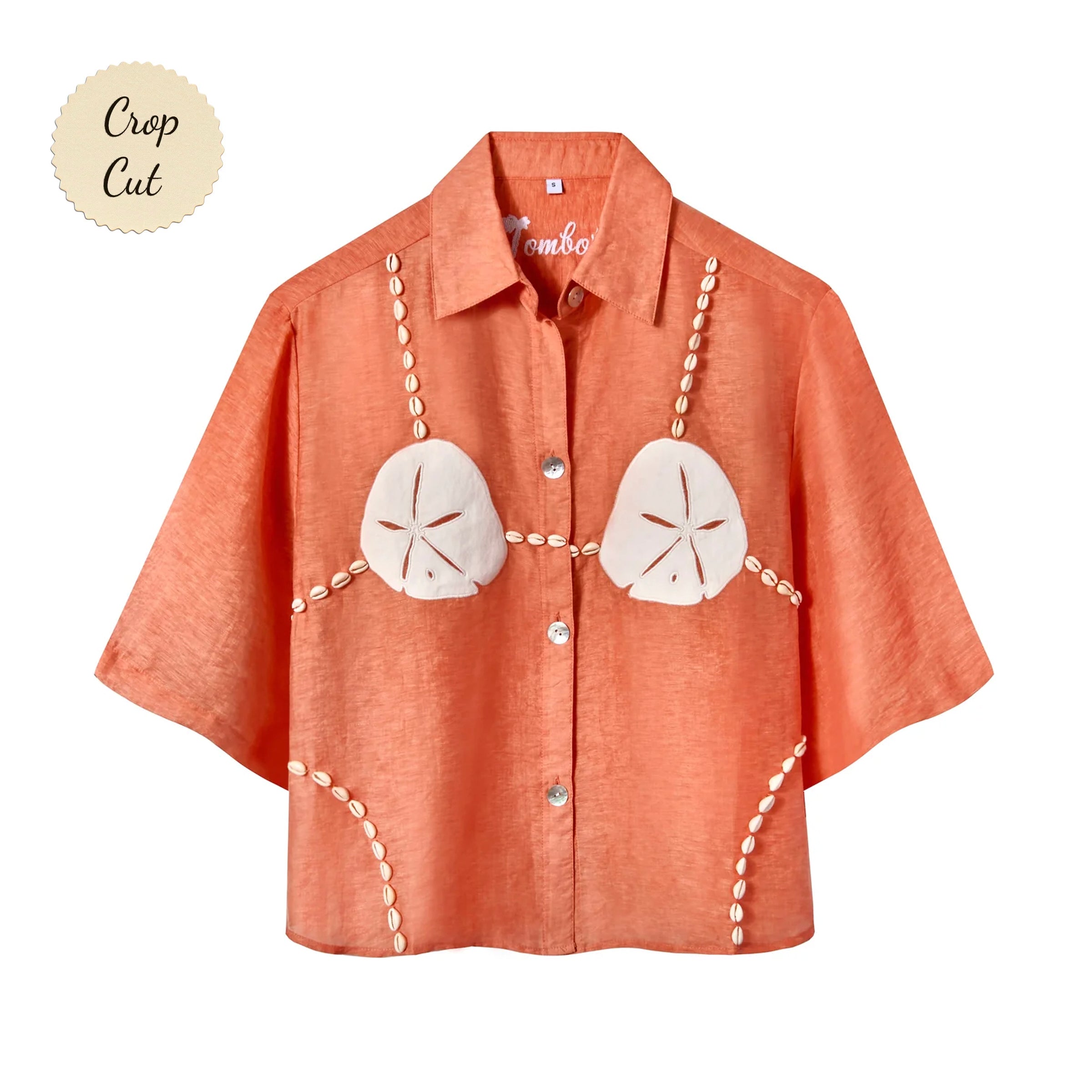 Orange short-sleeve button-up shirt with a relaxed fit. The shirt features an embroidered design resembling a sand dollar bikini top, with two large cream-colored sand dollars at the chest and shell bead strands extending from the shoulders, across the chest, and down the sides. Small sticker that reads "Crop Cut"