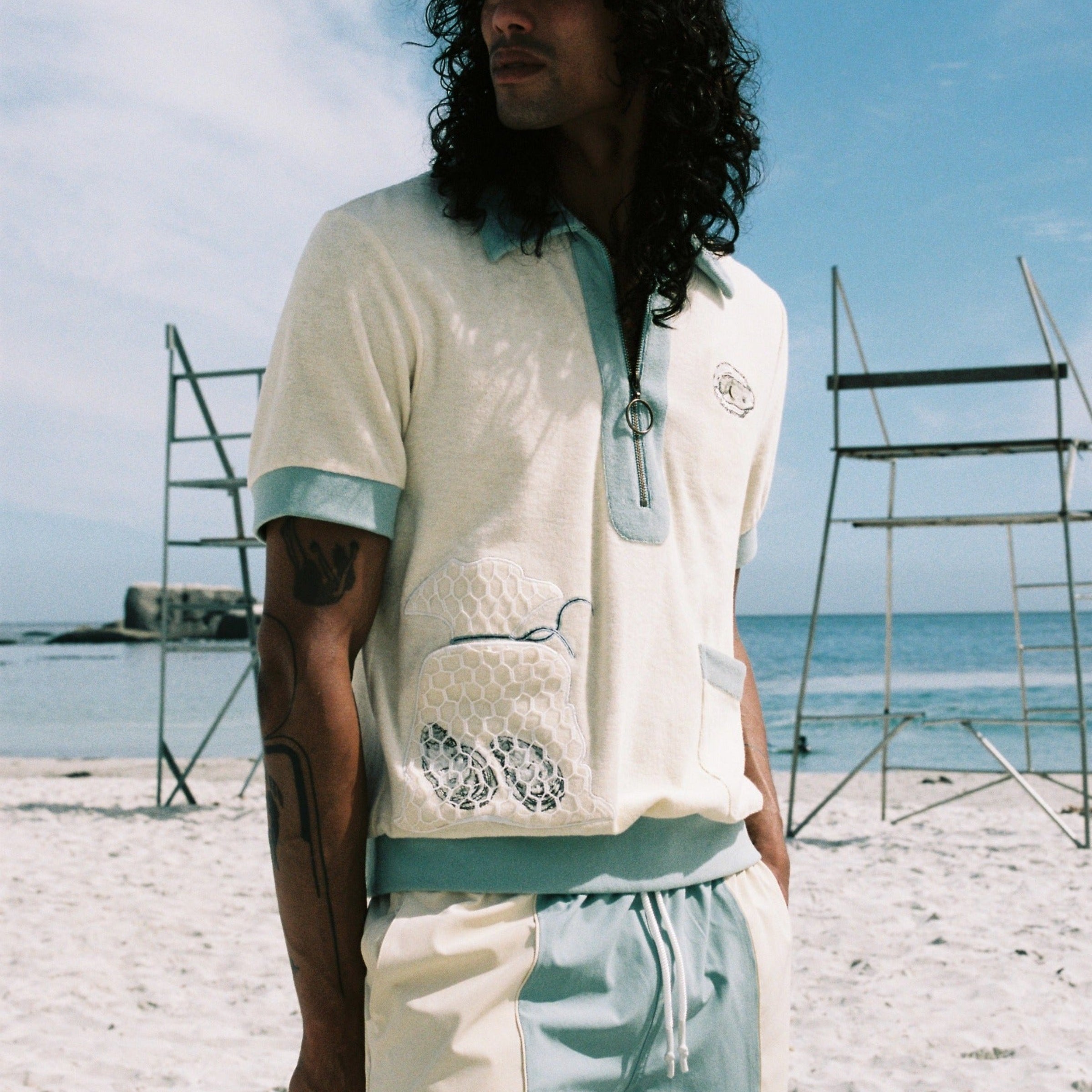 man wearing matching terry cloth oyster shirt with swim trunks looking off into the distance at the beach