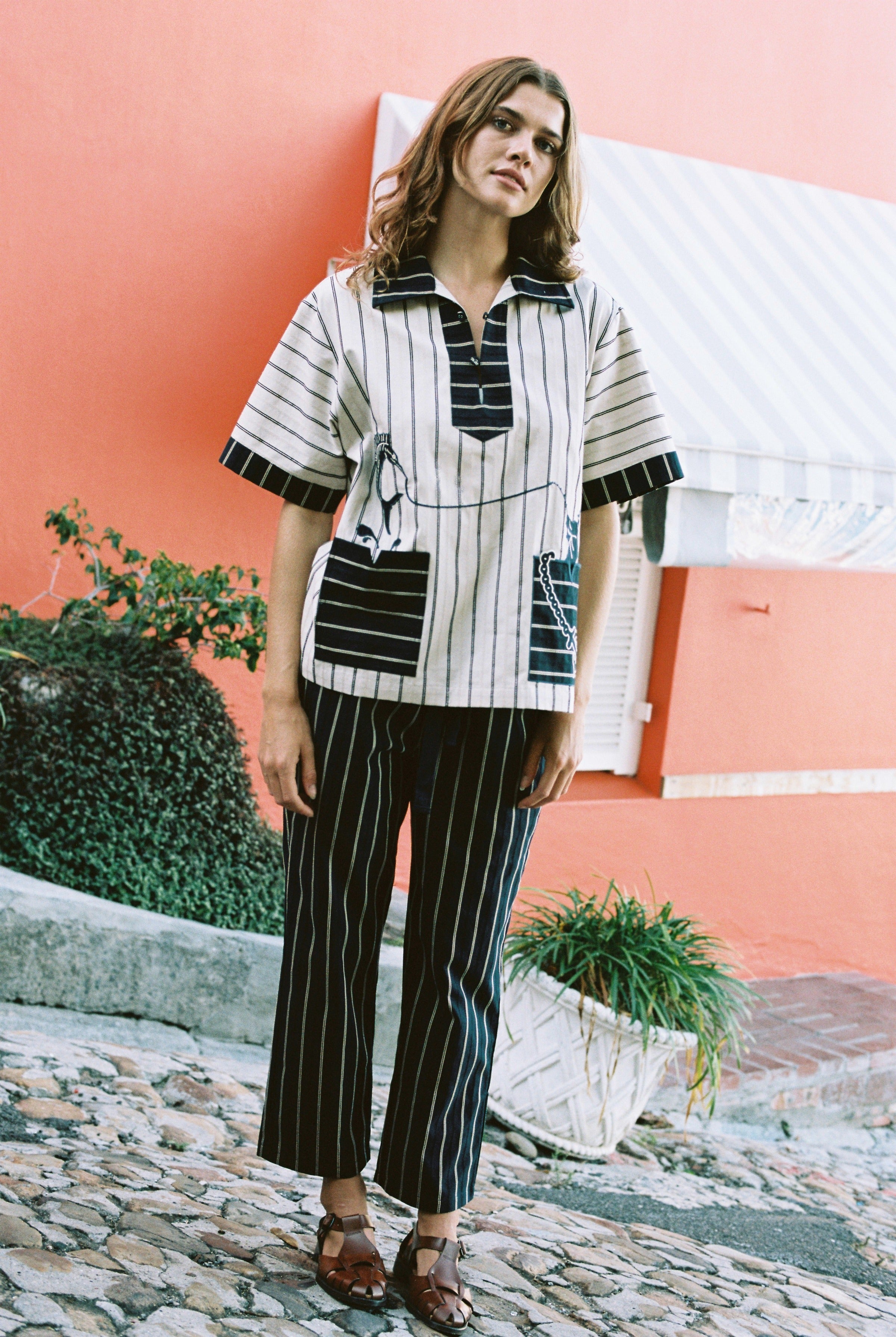 female model wearing Tombolo striped pop-over shirt with matching striped pants in front of a pink wall