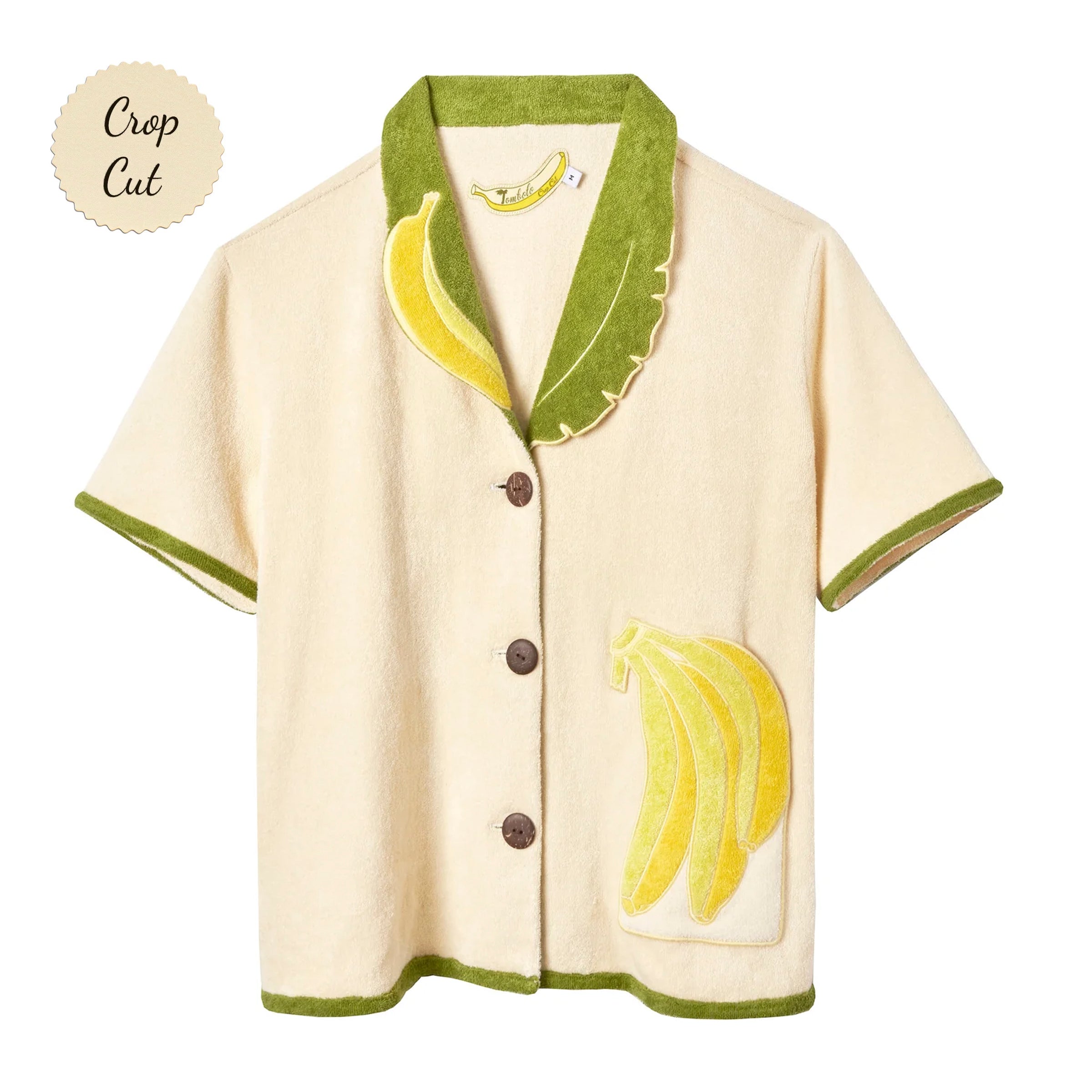 Short-sleeve cream terry cloth shirt with green trim, a green and yellow banana leaf collar, and a banana applique on the front pocket. Small sticker that reads "Crop Cut".