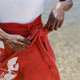 close up of woman at the beach wearing a white one piece bathing suit and tying the bow on her red skirt

