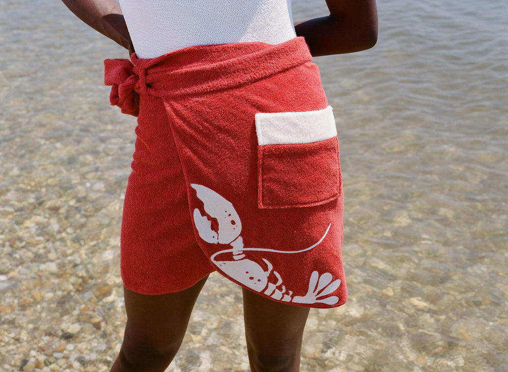close up of woman at beach wearing white bathing suit and red tie wrap skirt