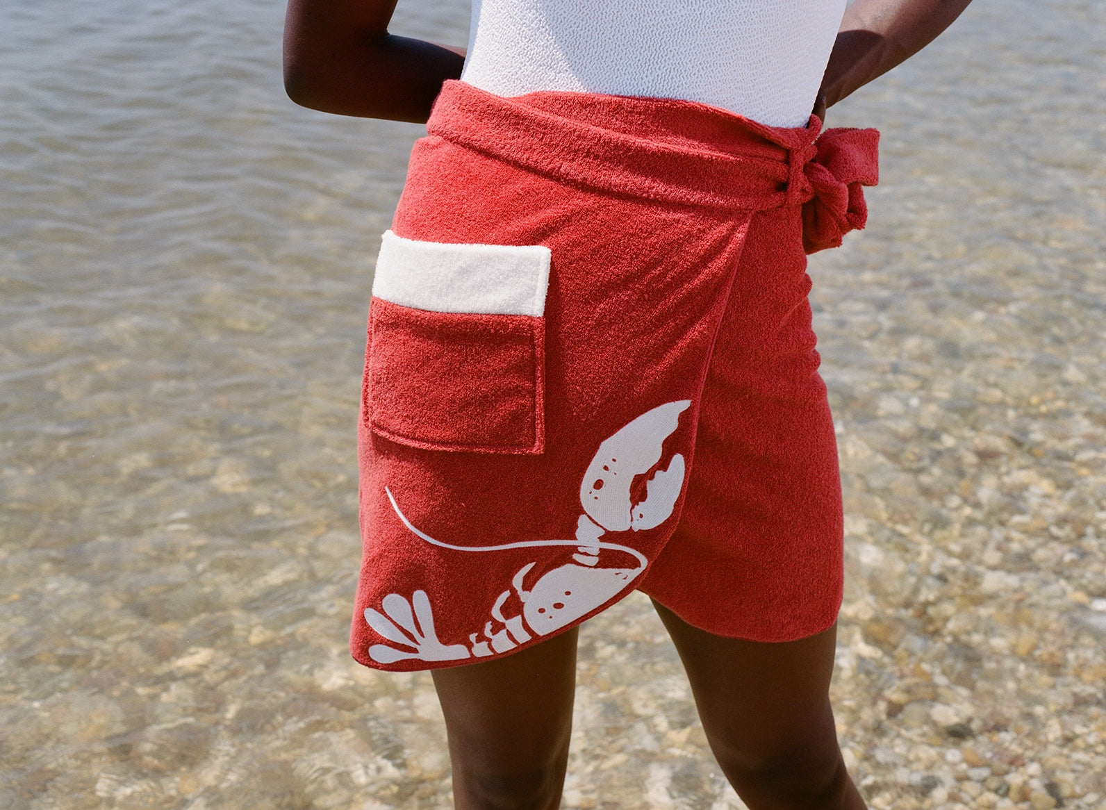close up of woman at beach wearing white bathing suit and red tie wrap skirt