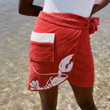 close up of woman at beach wearing white bathing suit and red tie wrap skirt