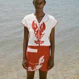 woman at beach wearing white lobster bib shirt and red skirt, looking straight at the camera 