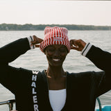 Woman wearing red and white striped knit beanie with a whaler patch, and the navy cardigan with vertical 'WHALER' lettering in white.