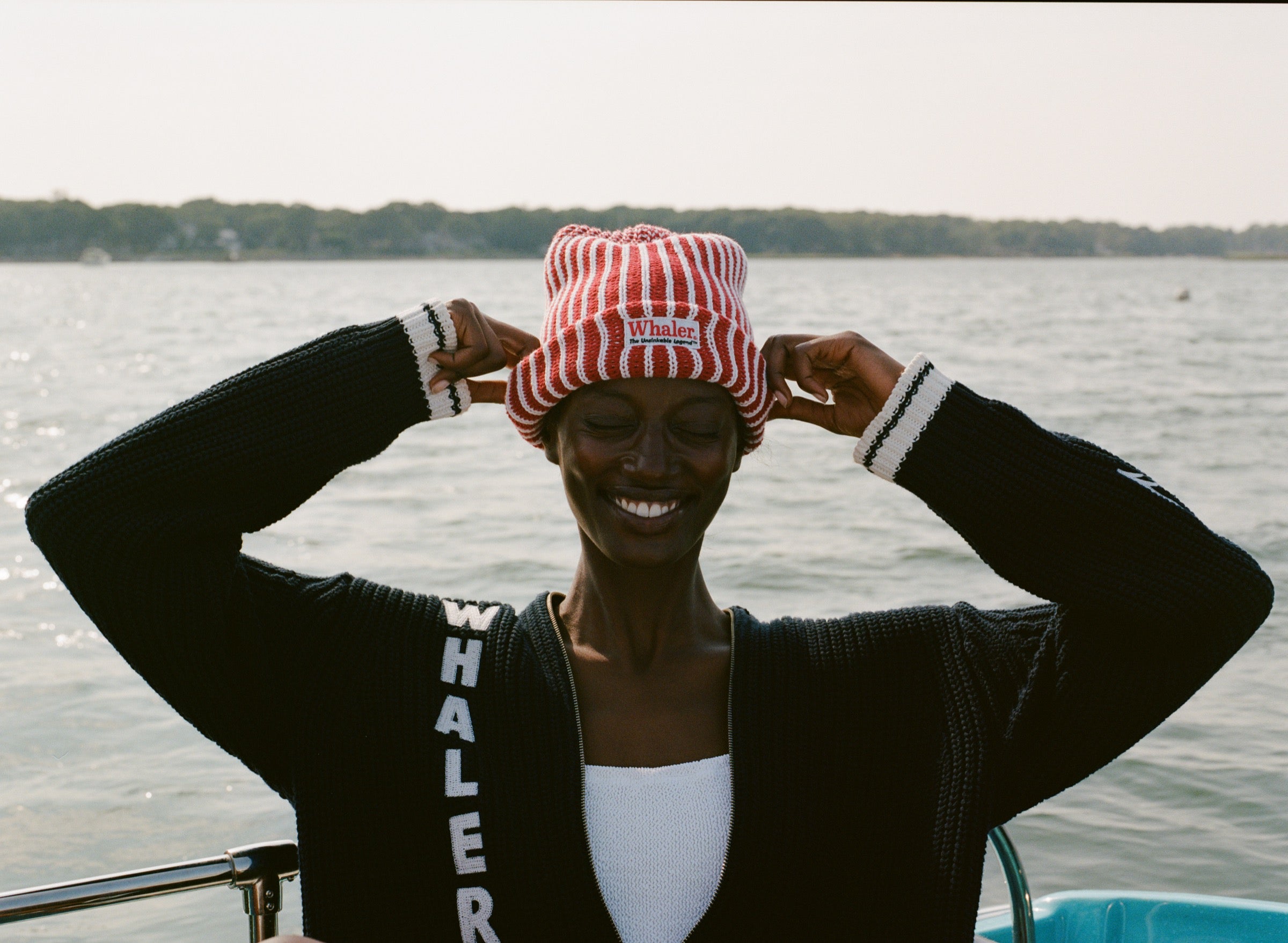Woman wearing red and white striped knit beanie with a whaler patch, and the navy cardigan with vertical 'WHALER' lettering in white.