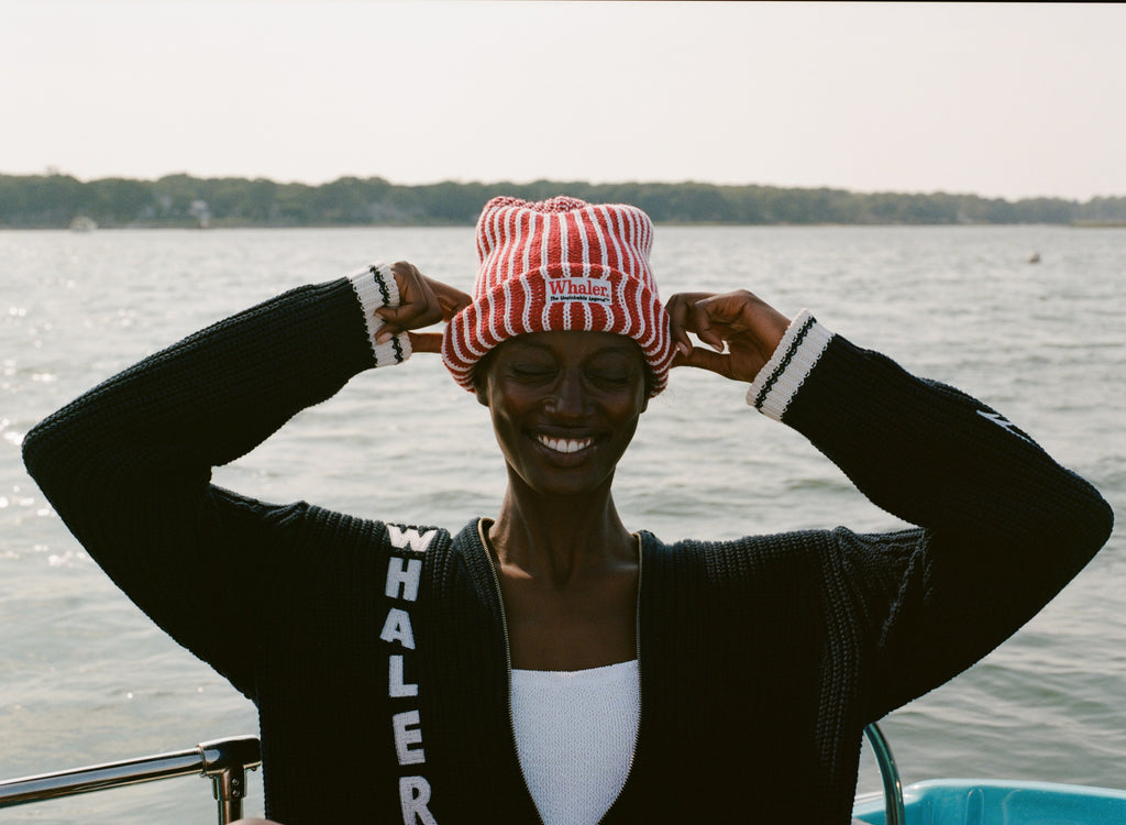 Woman wearing red and white striped knit beanie with a whaler patch, and the navy cardigan with vertical 'WHALER' lettering in white.