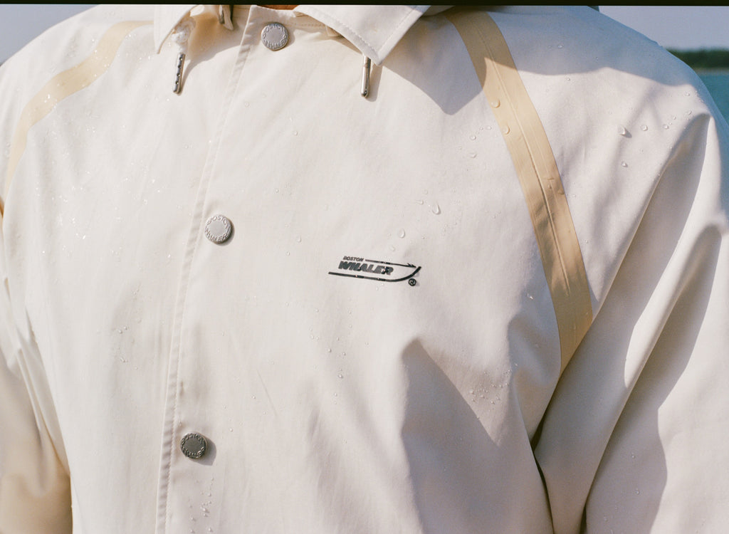 Close-up of a cream rain jacket with tan trim and 'Boston Whaler' logo.