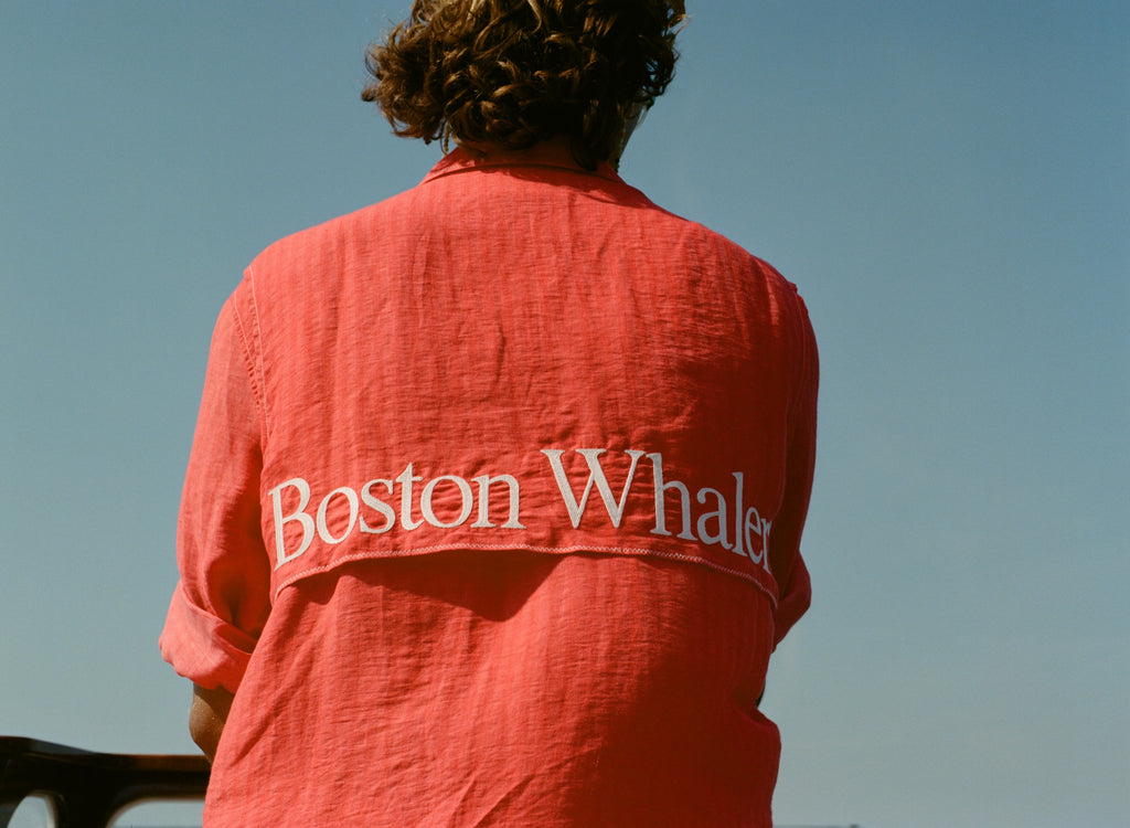 Back view of a person wearing a red button-up shirt with white embroidered text reading 'Boston Whaler' across the upper back.