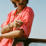 Man rolling up the sleeve of a red button-up shirt while leaning on a wooden boat railing.