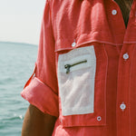 Close-up of the white mesh pocket with a small brass zipper on the red button down shirt. 