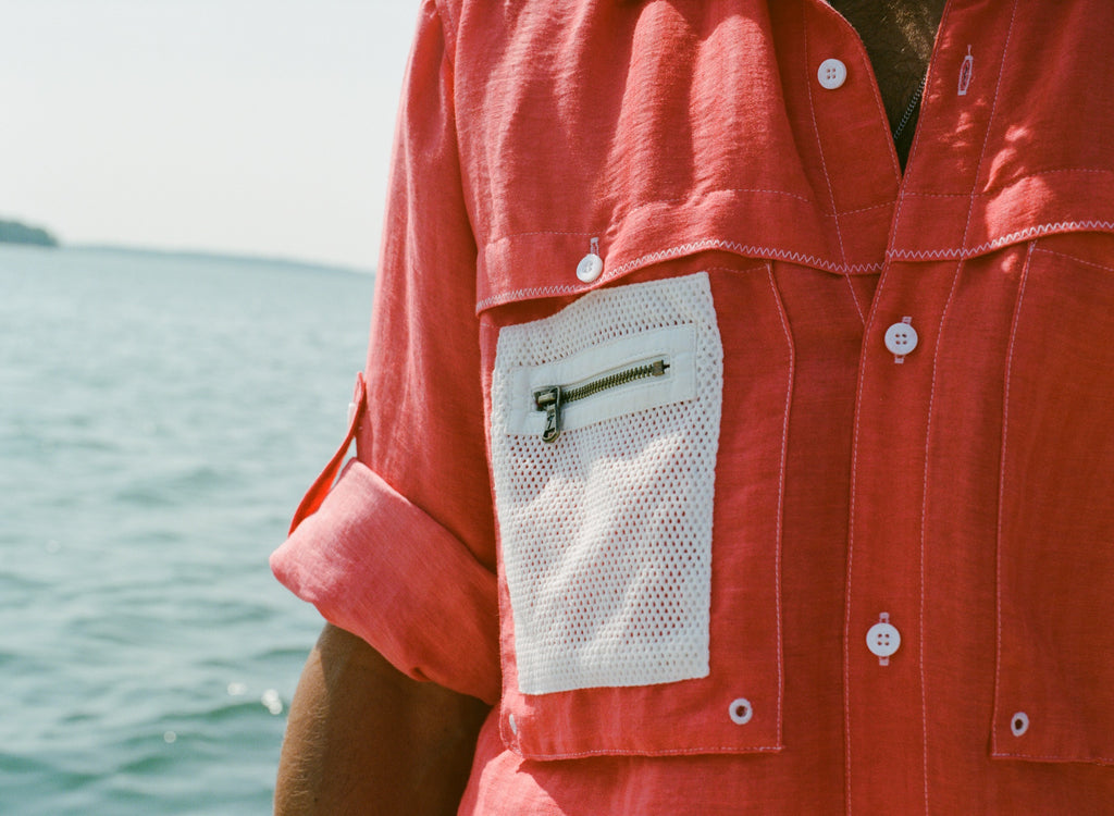 Close-up of the white mesh pocket with a small brass zipper on the red button down shirt. 