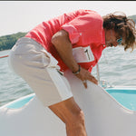 Man on a boat bending forward while adjusting a white cover. He wears two-tone khaki and off-white shorts with a side flap pocket and a red fishing shirt with a white mesh pocket.