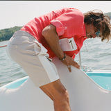 Man on a boat bending forward while adjusting a white cover. He wears two-tone khaki and off-white shorts with a side flap pocket and a red fishing shirt with a white mesh pocket.