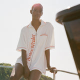 Woman sitting on the edge of a boat wearing a white terry short-sleeve zip up cabana with red 'Boston Whaler' text and red contrast stitching.