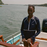 Woman wearing a navy sun shirt with white piping and a striped collar, standing at the helm of a boat.