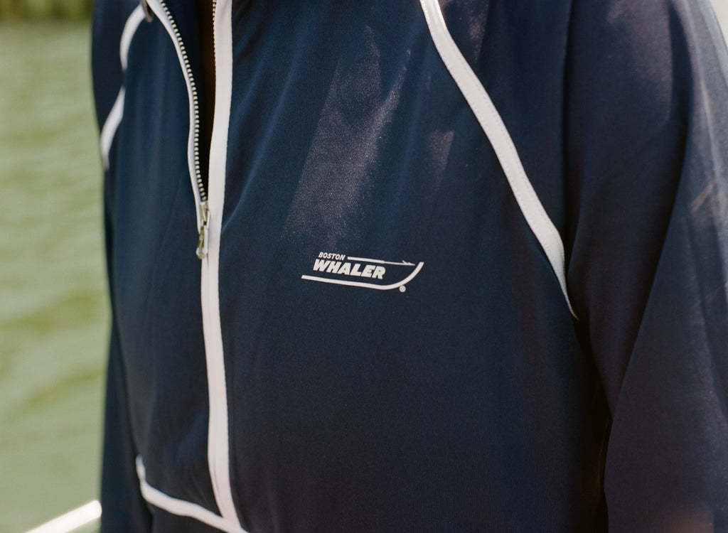 Close-up of the Boston Whaler logo on a navy sun shirt with white piping and a front zipper.