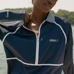 Close-up of a woman wearing a navy long-sleeve sun shirt with white piping and a striped collar. White embroidered text on the left chest reads 'Boston Whaler,' and 'Tombolo' is stitched on the sleeve.
