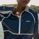 Close-up of a woman wearing a navy long-sleeve sun shirt with white piping and a striped collar. White embroidered text on the left chest reads 'Boston Whaler,' and 'Tombolo' is stitched on the sleeve.