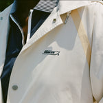 Close-up of a cream rain jacket with tan trim and Boston Whaler logo, worn over a navy top with a striped collar and white piping.